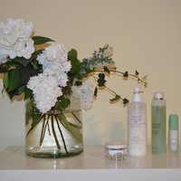 weißer Flieder in niedriger Vase mit Pflegeprodukten